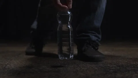 Man's hands leaving a bottle of crystal clear water on the floor in a low key Stock Footage 311175480