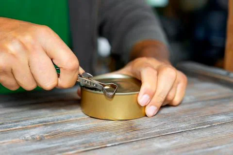 Man's hands open a tin can with an old rusty can opener with a metal handle Stock Photos