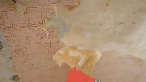 Mans hands in orange gloves removing old wallpaper from the wall, preparing the Stock Footage 329755830