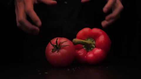 A man's hands pick up a red pepper and tomato on a dark background from the Stock-Footage 144370330