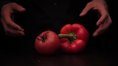A man's hands pick up a red pepper and tomato on a dark background from the Stock Footage 144370492