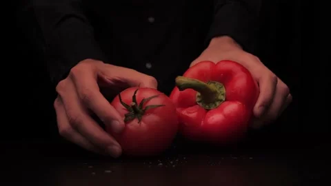 A man's hands pick up a red pepper and tomato on a dark background from the Stock-Footage 144370549
