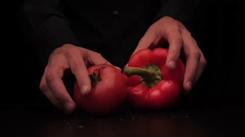 A man's hands pick up a red pepper and tomato on a dark background from the Stock-Footage 144370572