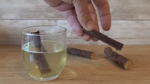 Man's hands place licorice root sticks into a glass of water on a wooden bo.. Stockbeeldmateriaal 340549274