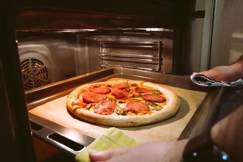 A man's hands pull out a homemade pepperoni pizza from the oven Stock Photos