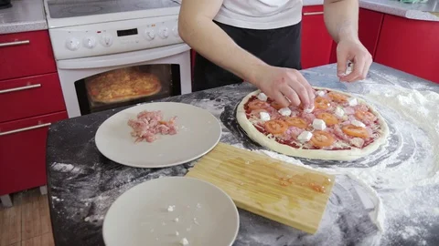 Man's hands put cheese on pizza with meat and tomato on a table with flour 스톡 동영상 128044451