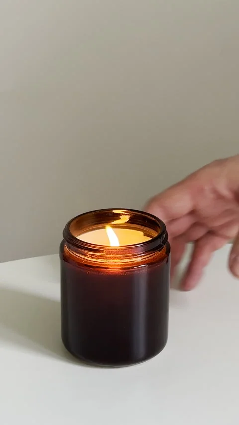 Man's hands puts burning candle in glass jar on white table, interior decorative Stock Footage 242617550