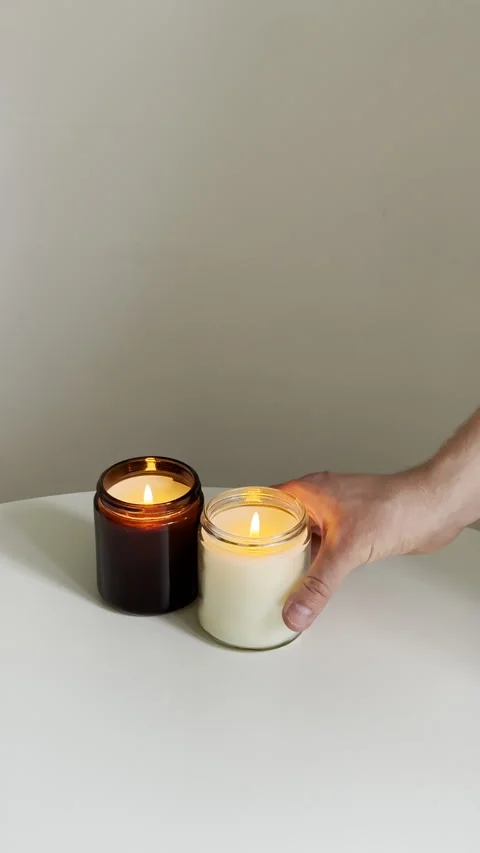 Man's hands puts burning candle in glass jar on white table, interior decorative Stock Footage 242618657