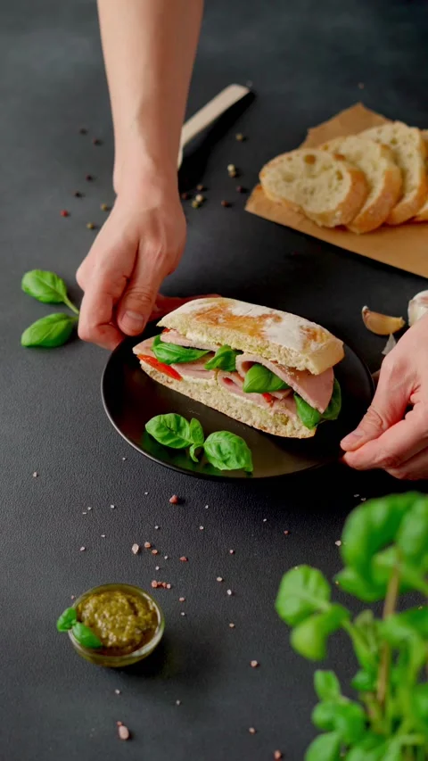 Man's hands puts plate of Chiabatta Sandwich with ham, basil, pesto on table Stock Footage 238533552