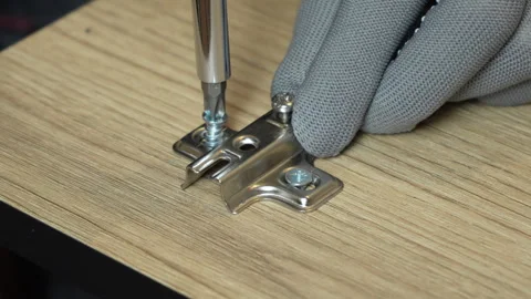Man's hands screw on the hinges for the cabinet door with a screwdriver Stock Footage 303472178