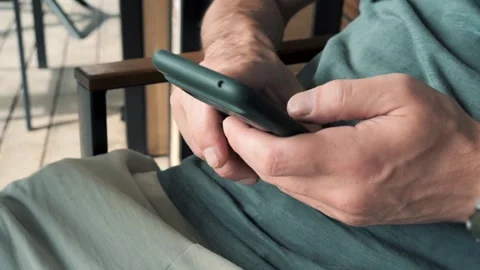 Man's hands scrolling a smartphone while relaxing on a patio on a sunny day. Vidéo 277886959
