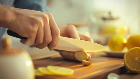 Mans hands skillfully slice a rhizome of fresh ginger releasing its pungent Stock Footage 331355631