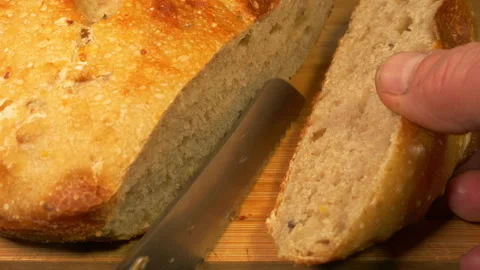 A man’s hands slicing the end off a loaf of crusty baked sourdough bread. Stock Footage 279084372