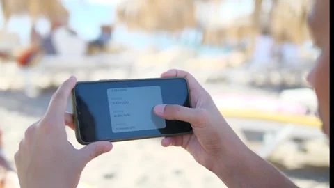 A mans hands on a sunny beach navigate a health application, scrolling through Stock-Footage 318644700