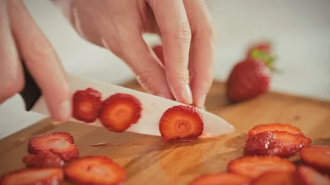 A mans hands thinly slice ripe red strawberries on a cutting board with a wh Stock Footage 346388524