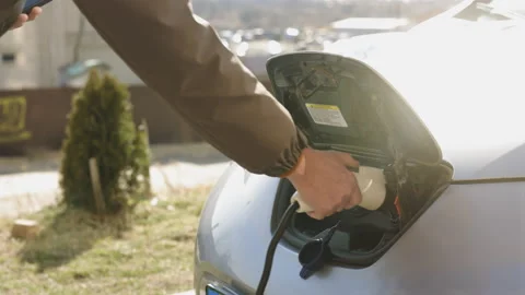 Man's hands unplugging her electric automobile. A shot under the hatch where the Stock Footage 196002534