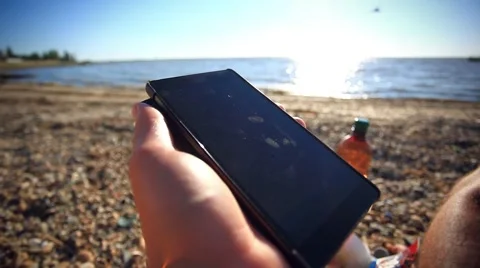 Man's hands uses mobile smartphone near the sea at sunset beach. With blurred Stock Footage 51698467