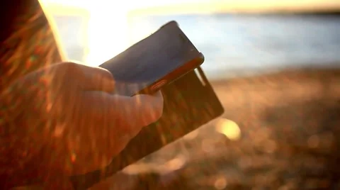 Man's hands uses mobile smartphone near the sea at sunset beach. With blurred Stock Footage 51720869