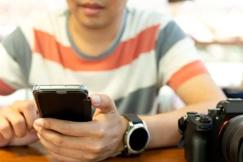 Man's hands using smart phone with DSLR camera on wooden table. Stock Photos