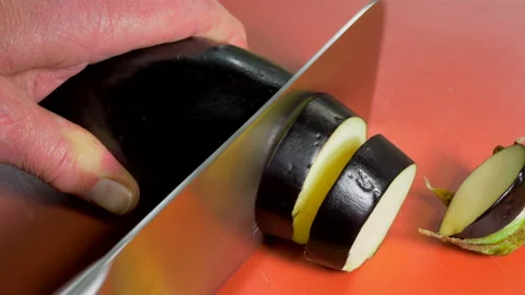 Man's hands using a steel cleaver to cut a raw aubergine into slices. Stock Footage 192390069