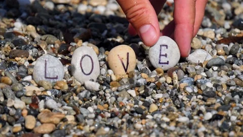 Man's hands will lay out the word love from sea stones with letters Stock Footage 138750936