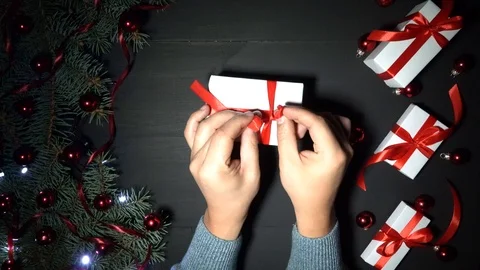 Mans hands wrap a gift. Black background of Xmas adorned with baubles and lights Stock Footage 99121661