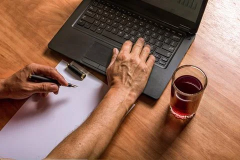 Man's hands write in ink on white paper and type on a laptop keyboard. A glas Foto stock