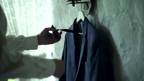 Man’s jacket and bow tie hangs on hanger on white wall. Groom takes bow tie. Stock Footage 139528791