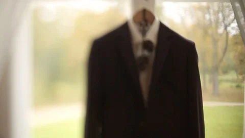 A man's jacket and suit hangs on a hanger before the groom's wedding hanging by Stock Footage 95301275