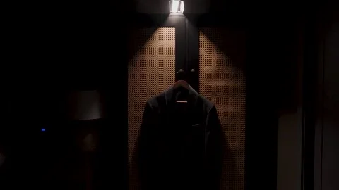 A mans jacket hangs on a hanger in a room with dim lighting from a lamp Stock Footage 329249033