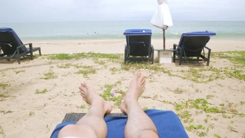 To man's legs, feet while relaxing on sunbed near beach in resort in thai Stock Footage 189949082