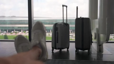Man's legs sitting in front of two luggage suitcases standing near the window at Stock Footage 280157961