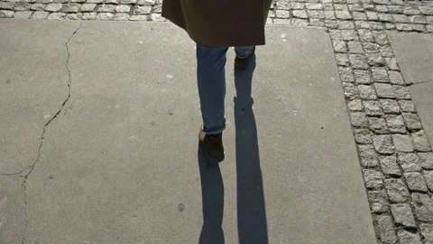 Man's walking legs in blue jeans, brown leather shoes and coat Stock Footage 106726776