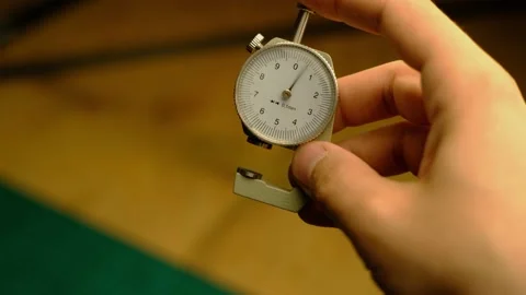 A man's white hand holds a thickness gauge for genuine leather Stock Footage 155382501
