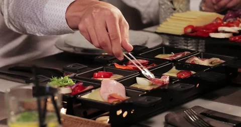 Man's woman's hand with help kitchen tongs are placed on top of salami raclettes Stock Footage 179026382