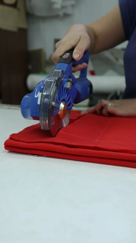 Manual cutting of red fabric with electrical rotary cutter in textile workshop Stock Footage 300204625