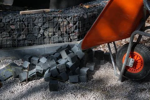 Manual unloading of granite cobblestone paver blocks from wheelbarrow Stock Photos