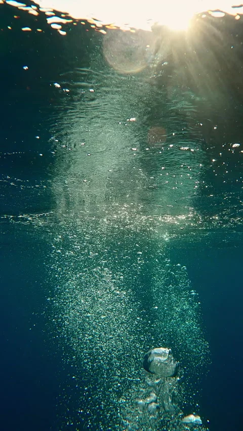 Many air bubbles rising to surface and reflecting in water, illuminated by Stock Footage 302766077