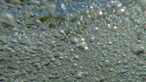 Many air bubbles rushing below surface of mountain river in front of blue sky, Stock Footage 316536678