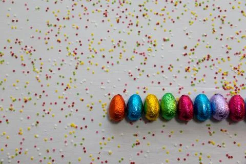 Many aligned colored chocolate easter eggs on white background and colorful c Foto stock