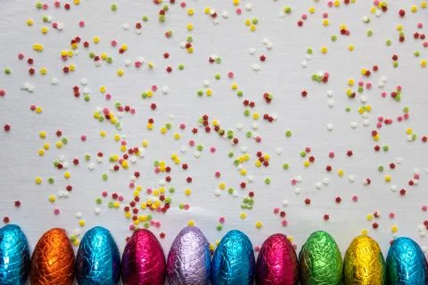 Many aligned colored chocolate easter eggs on white background and colorful c Stock Photos