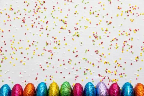 Many aligned colored chocolate easter eggs on white background and colorful c Stock Photos