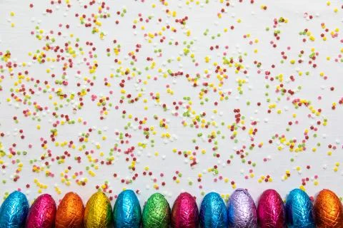 Many aligned colored chocolate easter eggs on white background and colorful c Stock Photos