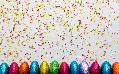 Many aligned colored chocolate easter eggs on white background and colorful c Stock Photos