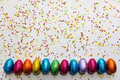 Many aligned colored chocolate easter eggs on white background and colorful c Stock Photos