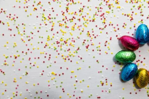Many aligned colored chocolate easter eggs on white background and colorful c Stock Photos