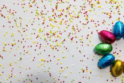 Many aligned colored chocolate easter eggs on white background and colorful c Stock Photos
