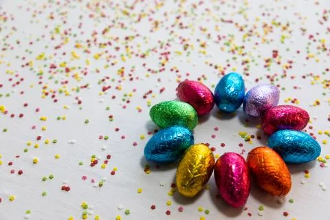 Many aligned colored chocolate easter eggs on white background and colorful c Stock Photos