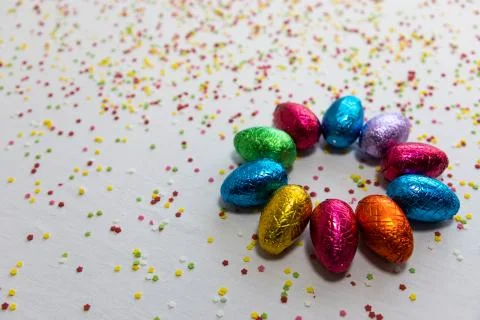 Many aligned colored chocolate easter eggs on white background and colorful c Stock Photos
