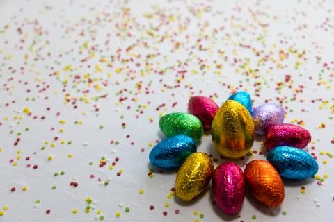 Many aligned colored chocolate easter eggs on white background and colorful c Stock Photos